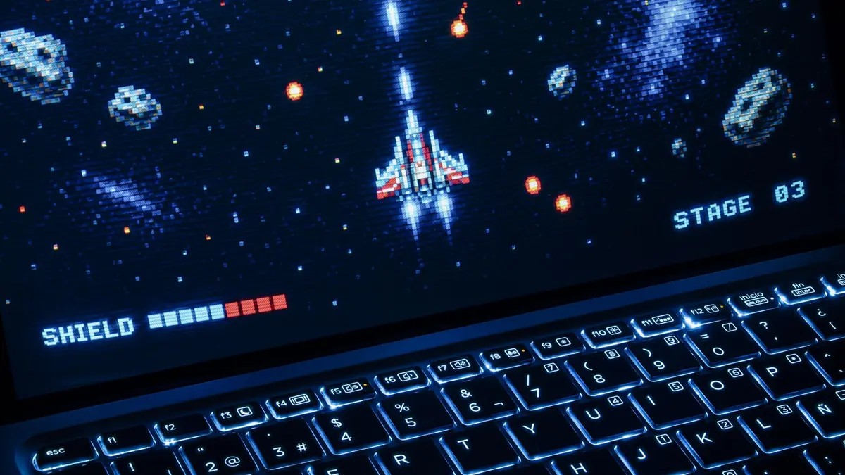A classic arcade space shooter game displayed on a laptop with illuminated keyboard, showing retro graphics.