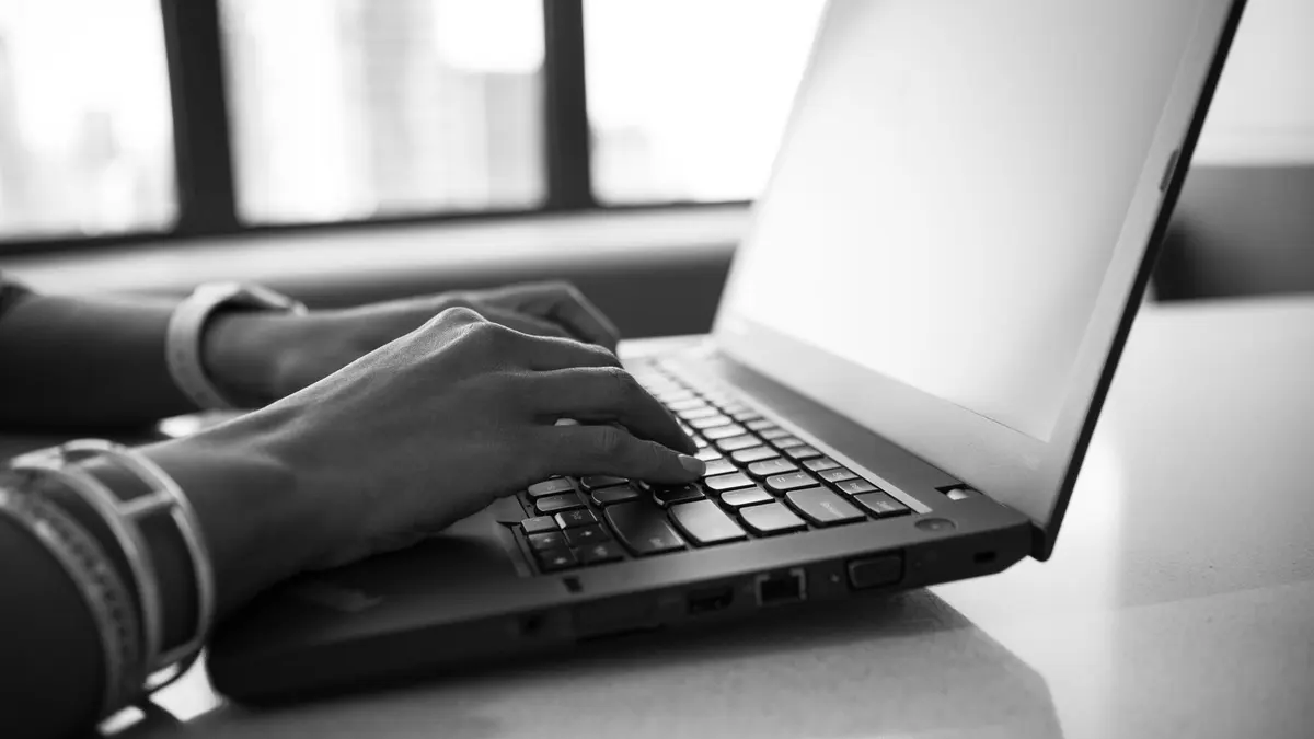 Close-up black and white photo showing hands typing on a laptop, emphasizing modern technology.