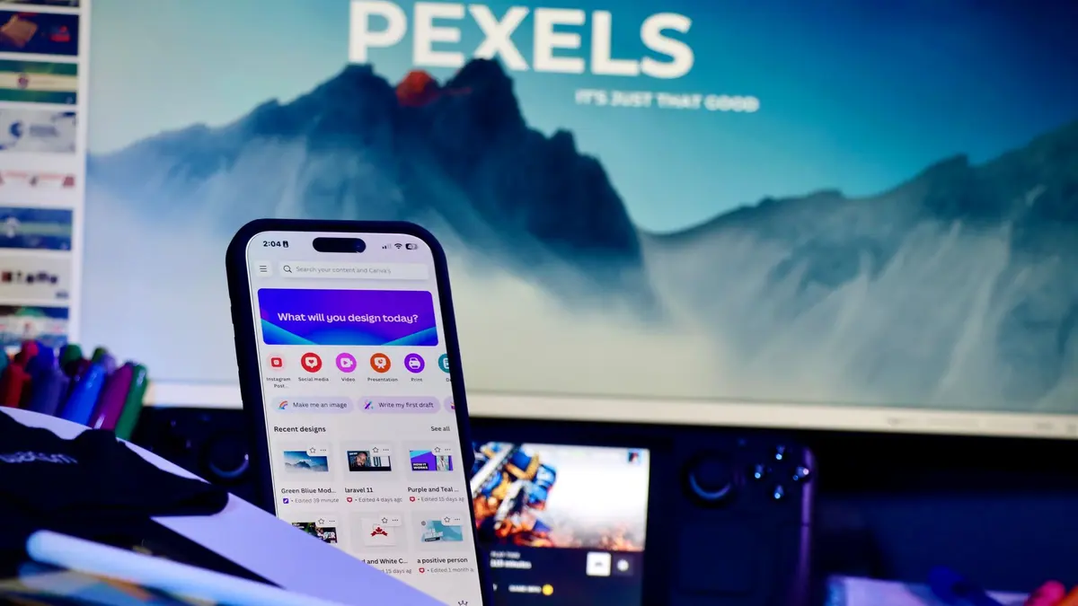 A creative workspace with a smartphone displaying design apps and a large monitor in the background.