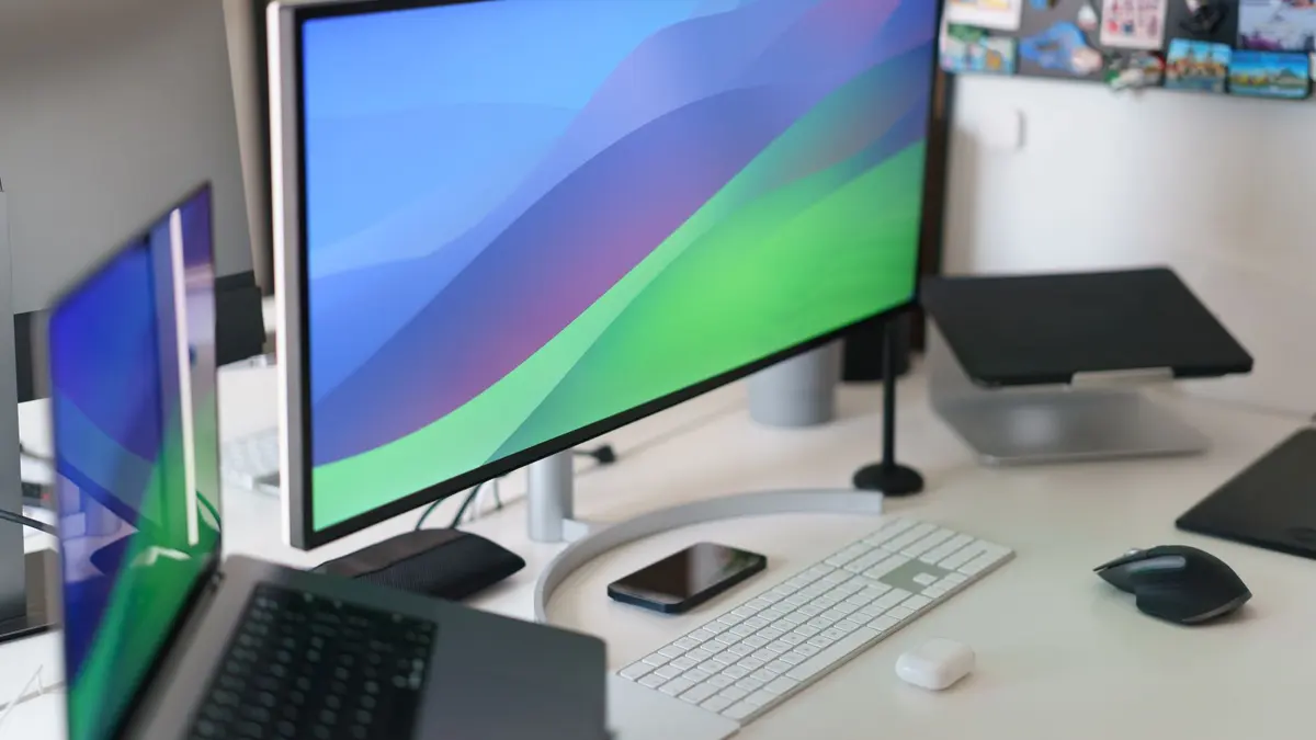 Sleek home office setup with multiple monitors, keyboard, smartphone, and stylish decor.