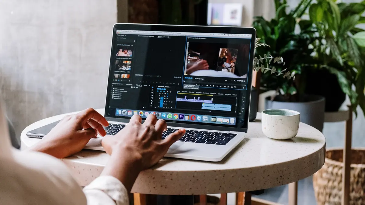 Freelance video editor working on a laptop in a cafe setting, utilizing Adobe software.