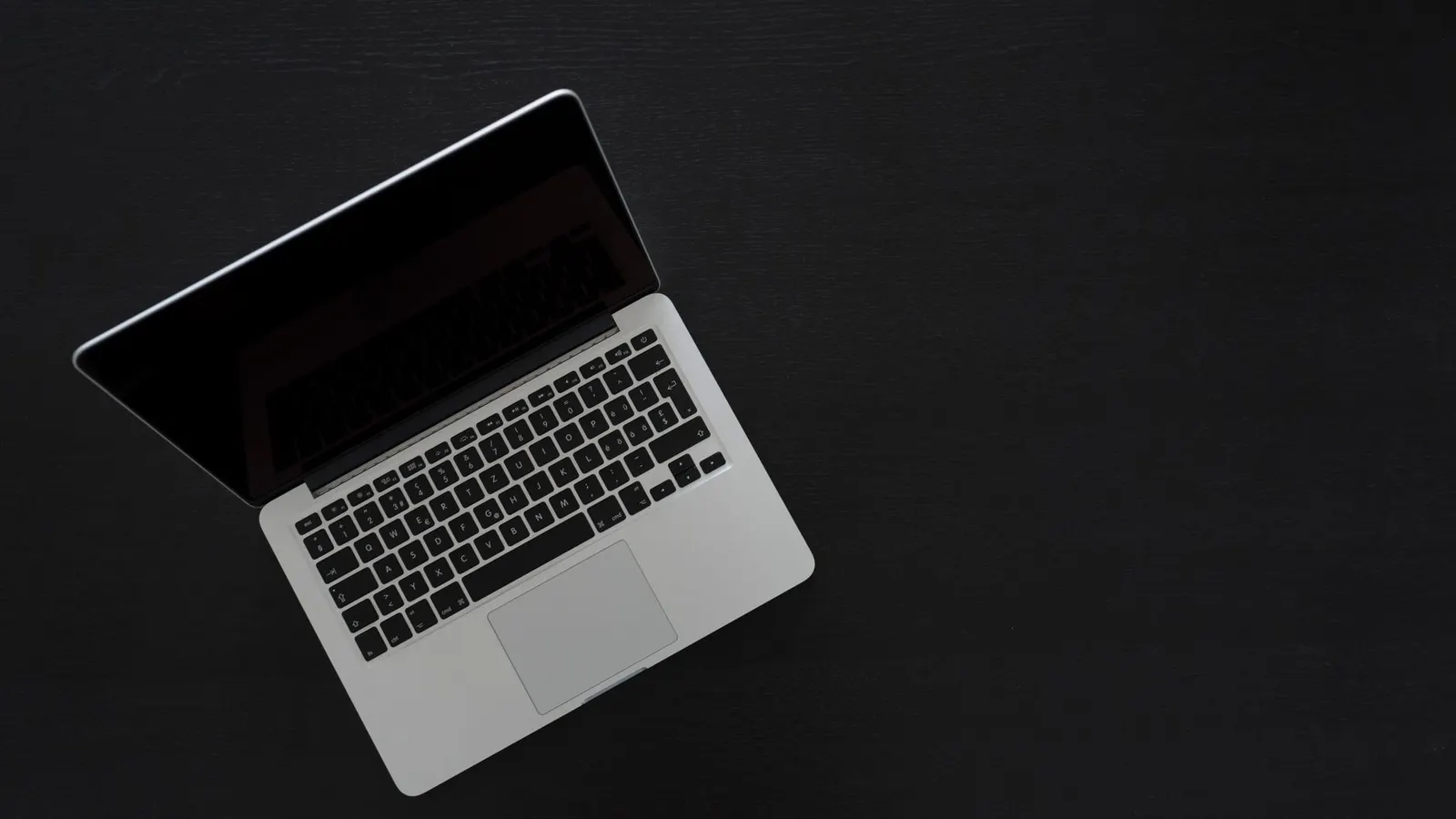 Overhead view of a MacBook laptop on a dark desk, showcasing modern technology and minimalism.